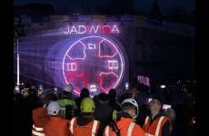 Grupa osób w roboczym ubraniu pracownika budowlanego obserwuje wyświetlany maping laserowy w formie słowa Jadwiga i obrazujący tarczę maszyny drążącej tunel kolejowy 