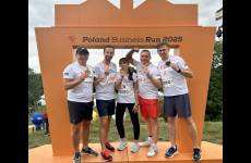 Grupa biegaczy z medalami w ręku na tle bramy z napisem Poland Business Run 2025