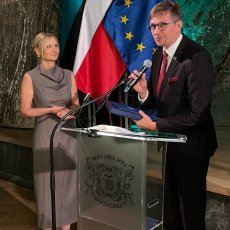 Mężczyzna przemawiający przy mównicy i przekazujący list i grawerton dyrektor krakowskiego oddziału KRUS